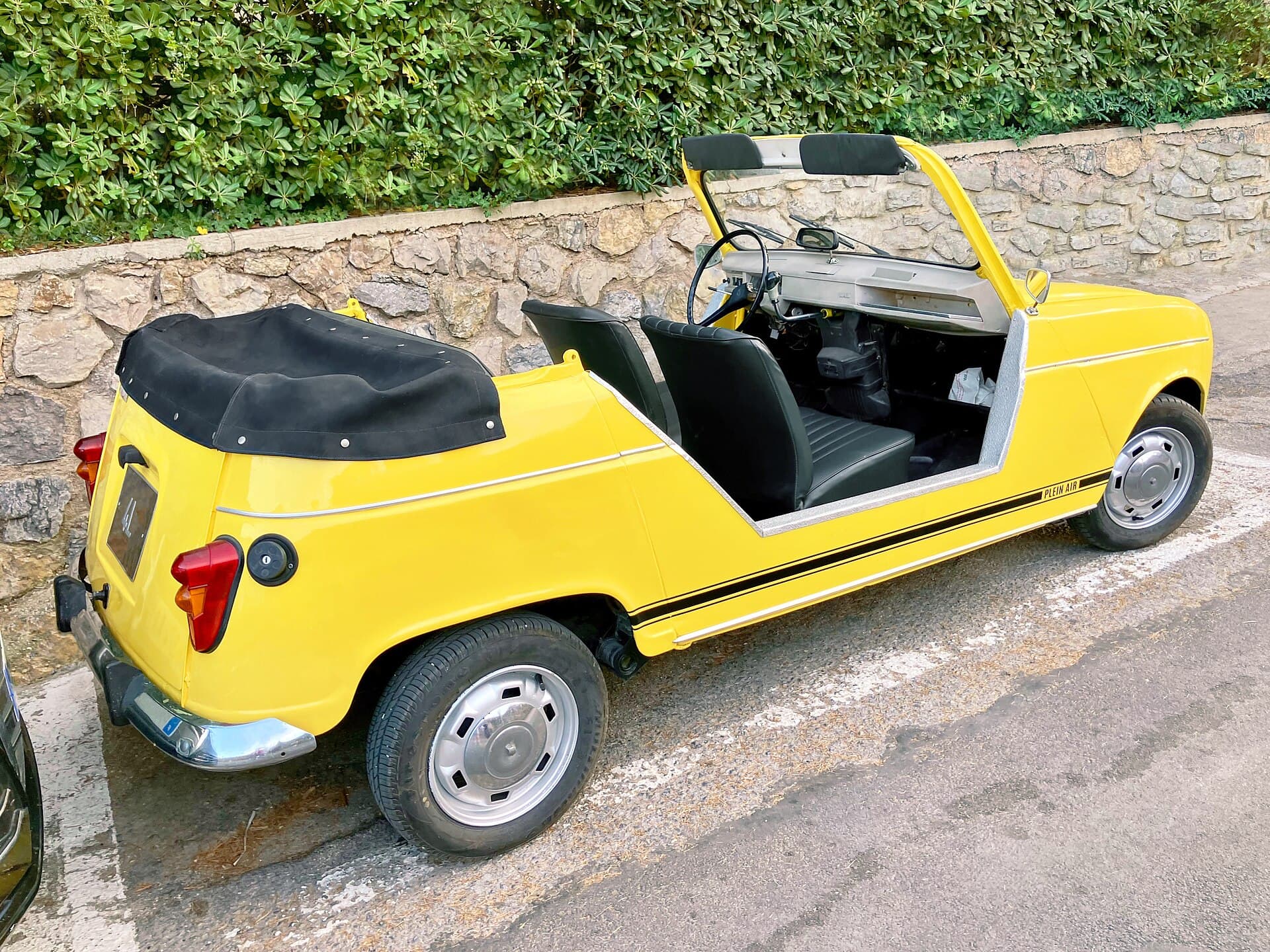 Ein gelber Renault 4 Plein Air, das offene Strandauto ohne Türen, vor einer Natursteinmauer