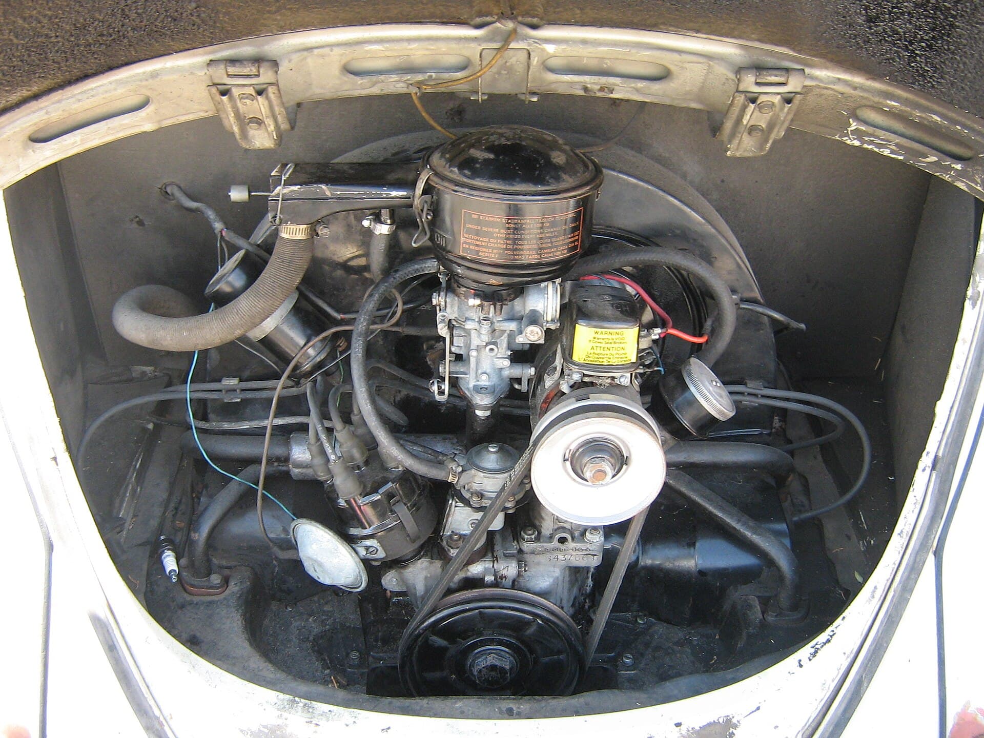 Alles, was ein Käfer zum Fahren braucht, auf einen Blick: Gebläse, Vergaser, Verteiler, Lichtmaschine. Ohne Kühler, ohne Steuergerät, ohne Überraschung. Foto: dave_7, Wikimedia Commons, CC BY 2.0, skaliert. Der Motorraum eines Käfers von 1962 mit dem luftgekühlten Boxer, Vergaser, Luftfilter und Lichtmaschine