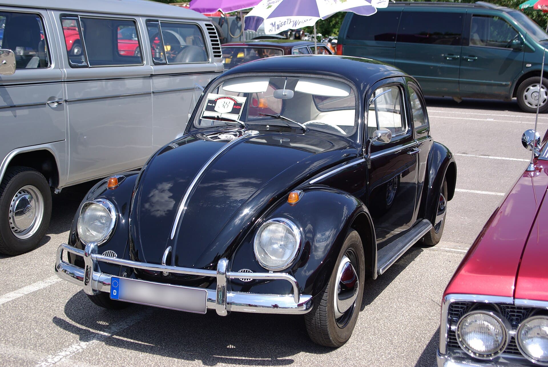 Ein Käfer der 1960er Jahre auf einem Treffen 2013, mit Startnummer hinter der Scheibe. Auf solchen Plätzen entsteht das Netzwerk, das Einsteiger tragen. Foto: Berthold Werner, Wikimedia Commons, CC BY-SA 3.0, skaliert. Ein schwarzer Käfer der 1960er Jahre mit Rallyeschild hinter der Scheibe auf einem Oldtimertreffen, daneben ein Bulli