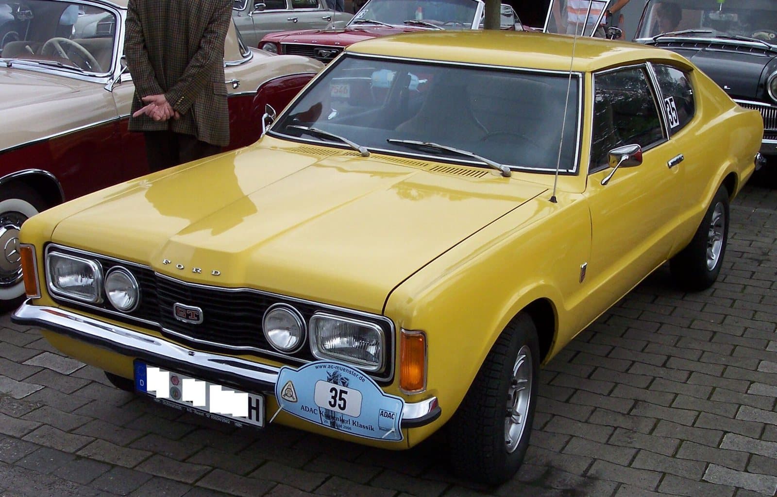 Ein Taunus 2.0 Coupé von 1972 mit Knudsen-Nase. Das Coupé mit Fließheck gab es nur in Deutschland. Foto: Stahlkocher, Wikimedia Commons, CC BY-SA 3.0, skaliert. Ein gelbes Ford Taunus 2.0 Coupé von 1972 schräg von vorn