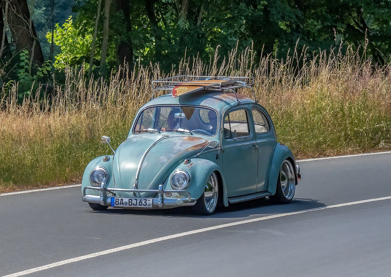 Ein Käfer mit Dachträger auf dem Weg zum Treffen, so reisen viele zum Küstendrive. Das Foto entstand 2022 beim Oldtimertreffen in Kulmbach. Foto: Ermell, Wikimedia Commons, CC BY-SA 4.0, skaliert. Ein grüner VW Käfer mit Dachträger und Surfbrett auf einer Landstraße