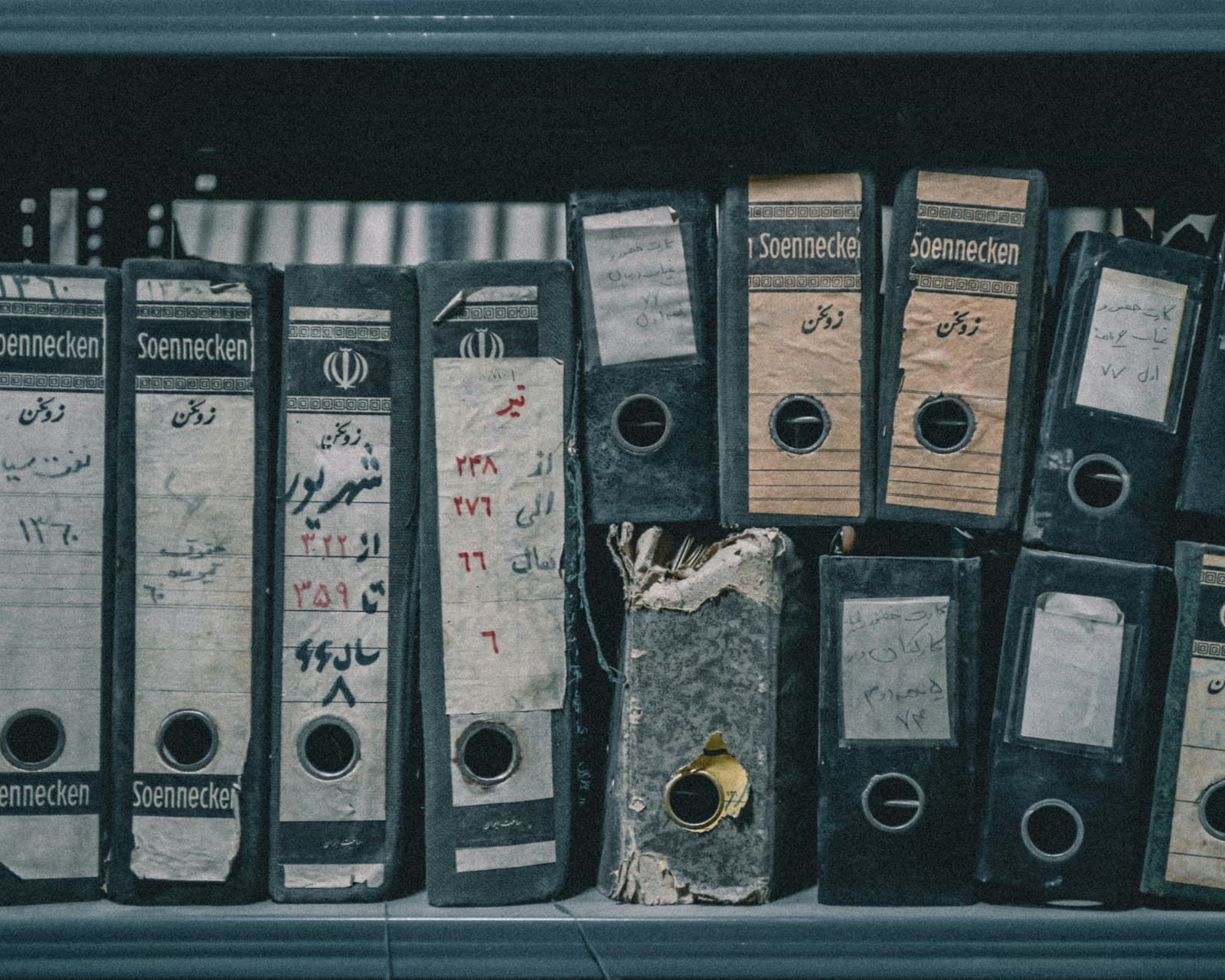 Die Geschichte eines Klassikers liegt selten an einem Ort. Ein Teil steht im Werksarchiv, ein Teil im Ordner des Vorbesitzers, ein Teil im Gedächtnis der Menschen, die ihn gefahren haben. Foto: Mota Ehdaei, Unsplash. Abgegriffene Aktenordner in einem staubigen Regal