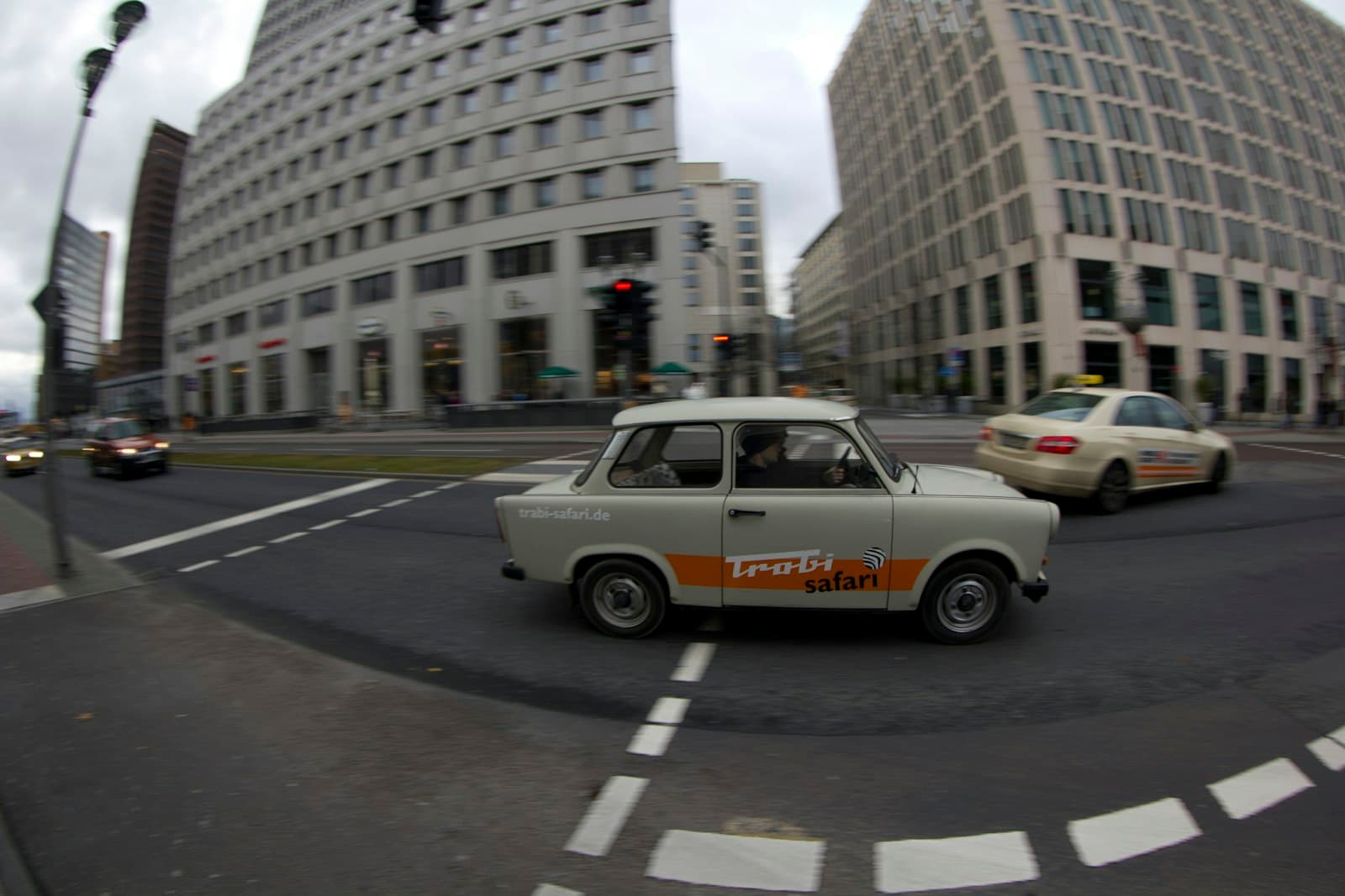 Ein Trabant der Trabi-Safari am Potsdamer Platz, wo bis 1989 der Mauerstreifen lag. Foto: Simon Infanger, Unsplash. Ein Trabant 601 der Trabi-Safari fährt über eine Kreuzung am Potsdamer Platz in Berlin