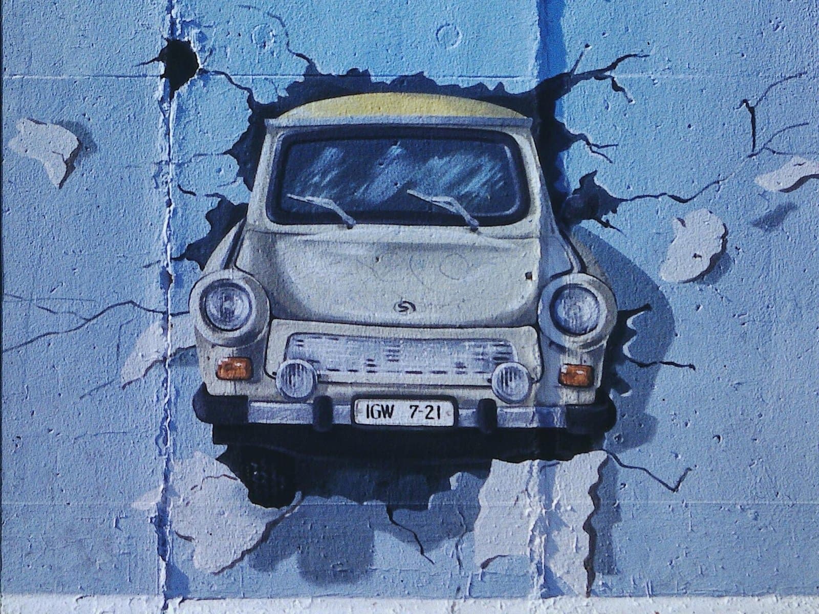 „Test the Best“ von Birgit Kinder, 1990 an die East Side Gallery gemalt: der Trabi, der durch die Mauer fährt. Foto: Jörg Fuhrmann, Wikimedia Commons, CC BY-SA 4.0, zugeschnitten und skaliert. Das Wandbild Test the Best von Birgit Kinder an der East Side Gallery, ein Trabant bricht durch die Mauer