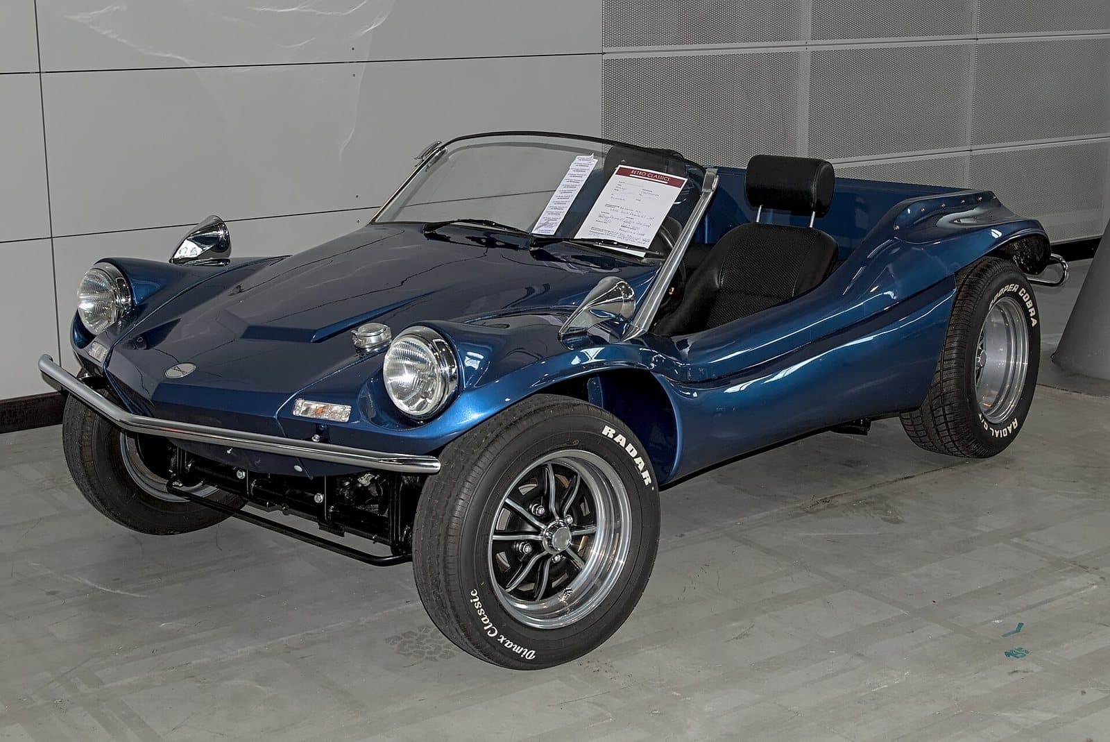 Ein Deserter GT von 1973 auf der Retro Classics 2025. Foto: Alexander Migl, Wikimedia Commons, CC BY-SA 4.0, skaliert. Ein dunkelblauer Deserter GT von 1973 mit flacher Front in einer Messehalle