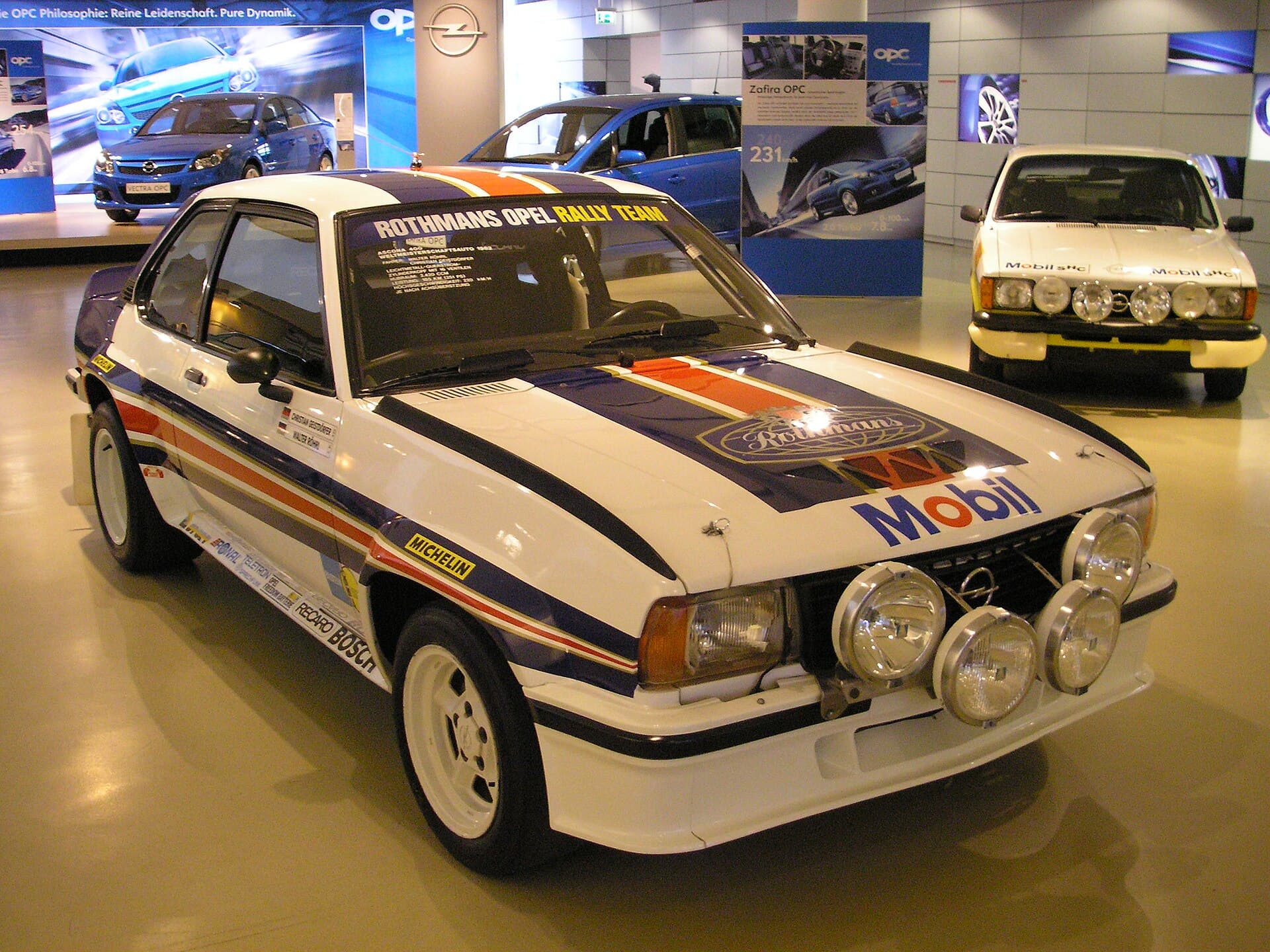 Der Ascona 400 in Rothmans-Farben, wie ihn Walter Röhrl 1982 zum Titel fuhr. Von der Straßenversion mit 144 PS entstanden 268 Stück. Foto: Gryffindor, Wikimedia Commons, gemeinfrei, skaliert. Walter Röhrls Opel Ascona 400 in den Farben von Rothmans in einer Ausstellung