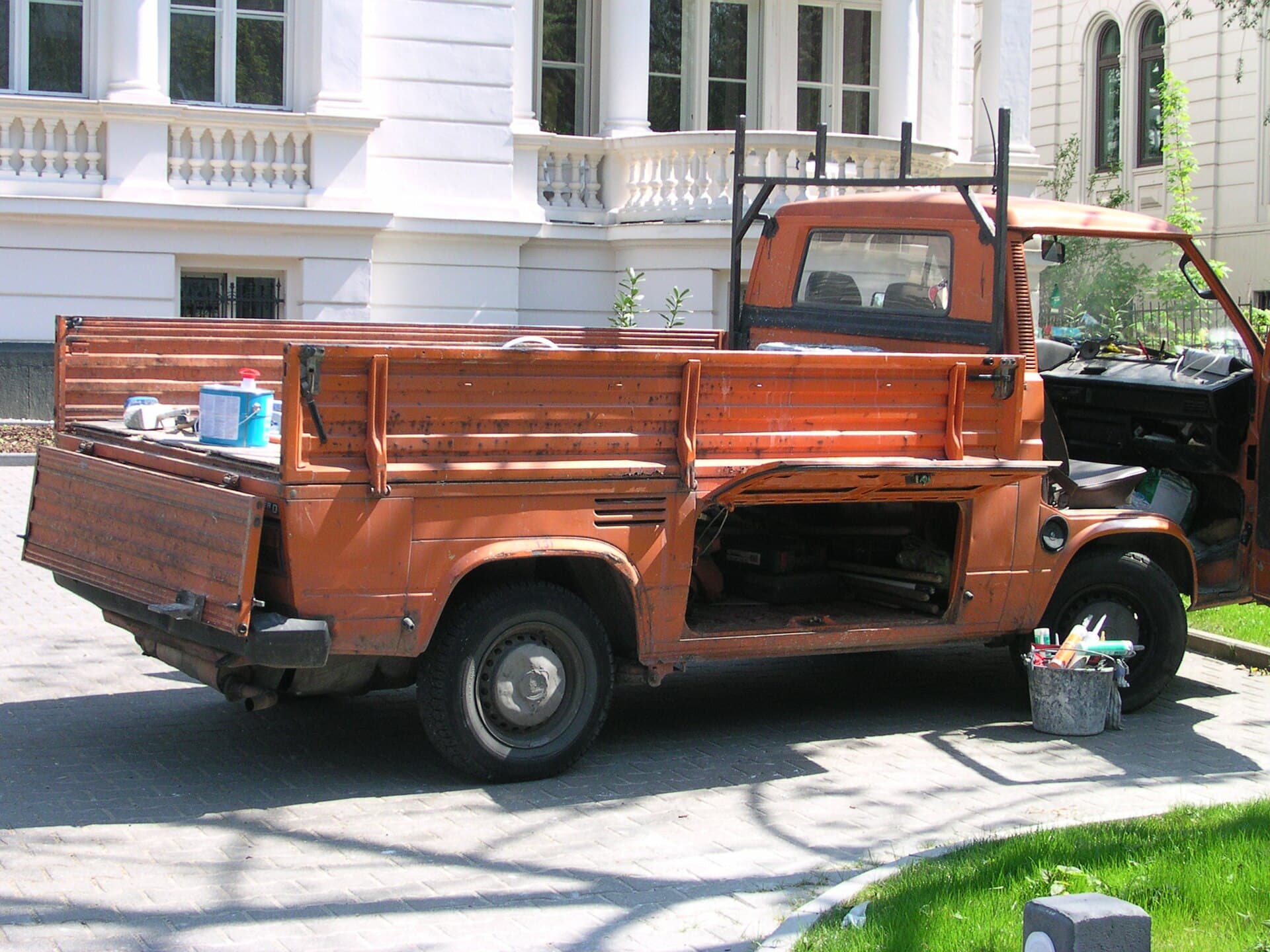 Was unter der Pritsche steckt: die Staukästen zwischen den Achsen, die Halter der Bordwände und das Riffelblech. Genau hier beginnt die Besichtigung. Foto: Norbert Schnitzler, Wikimedia Commons, CC BY-SA 3.0, skaliert. Eine orange T3 Pritsche mit heruntergeklappten Bordwänden und geöffneten Staukästen unter der Ladefläche