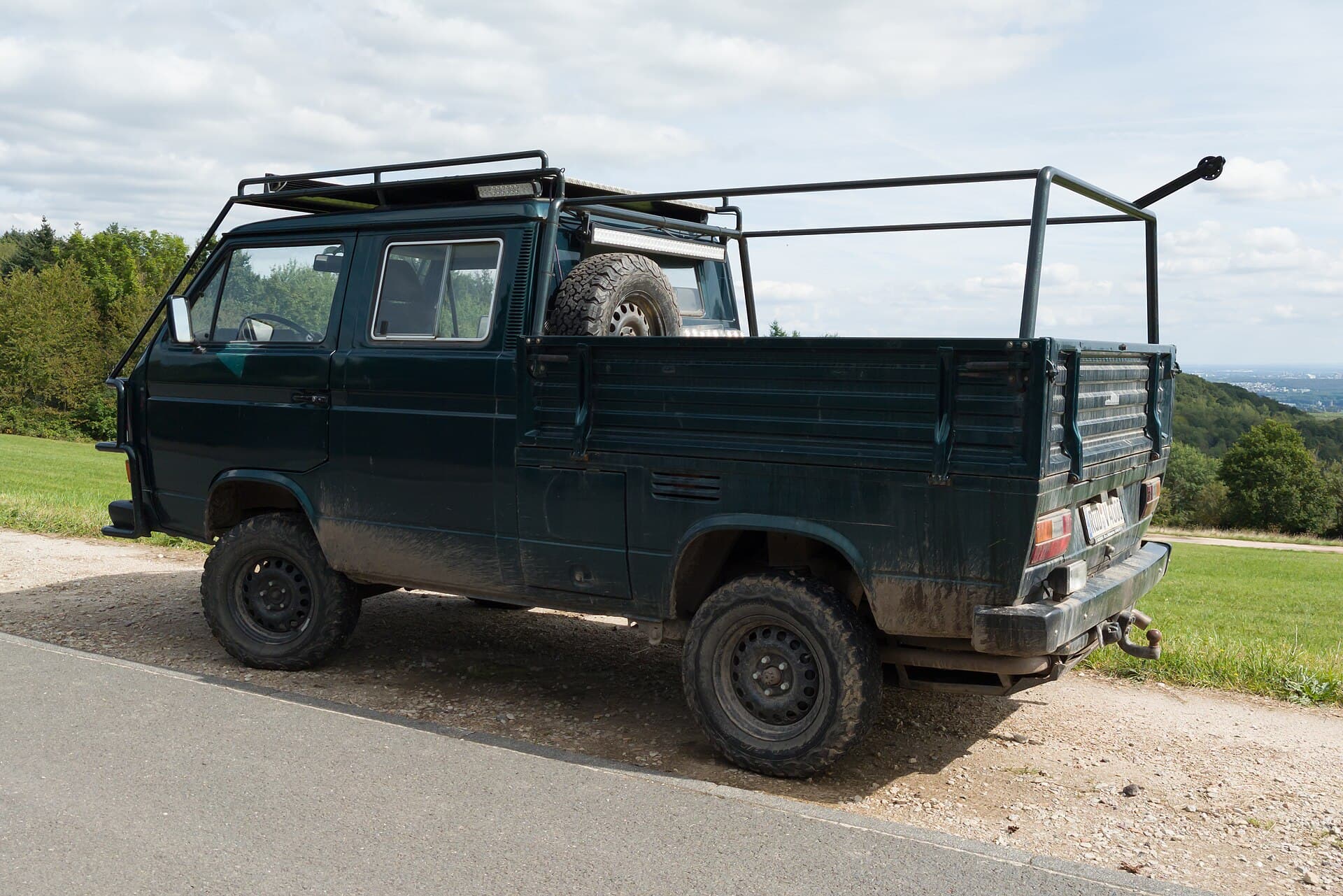 Eine Syncro-Doka auf 16 Zoll, mit den Kotflügelverbreiterungen und der Bodenfreiheit, die den 16-Zöller zum gesuchtesten offenen T3 machen. Foto: Matti Blume, Wikimedia Commons, CC BY-SA 4.0, skaliert. Eine dunkelgrüne T3 Doka Syncro auf 16-Zoll-Rädern mit Gestell über der Ladefläche