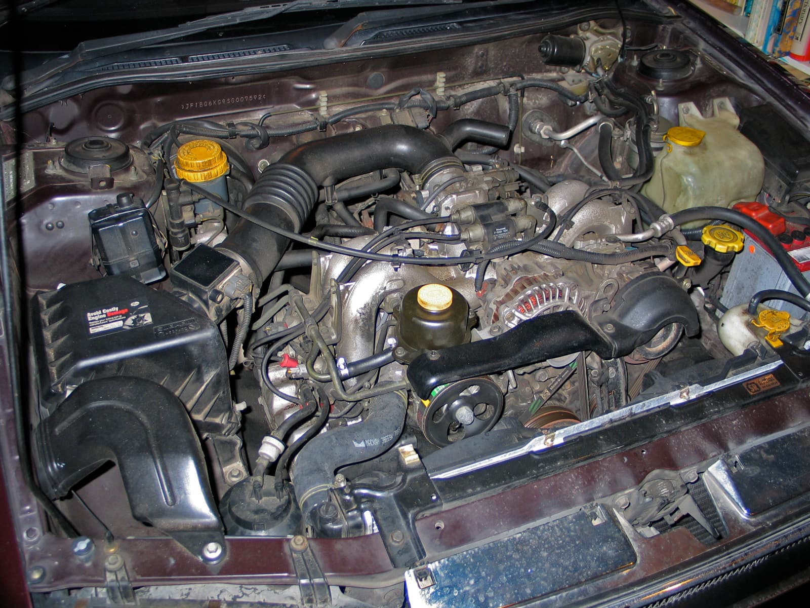 Der Subaru EJ22: ein wassergekühlter Boxer wie der VW-Motor, nur mit 136 PS. Im T3 braucht er eigene Kühlung, Ansaugung und Servoleitung. Foto: DucksnakeNZ, Wikimedia Commons, gemeinfrei, skaliert. Ein Subaru-Boxer EJ22 im Motorraum, mit Ansaugung und Riementrieb